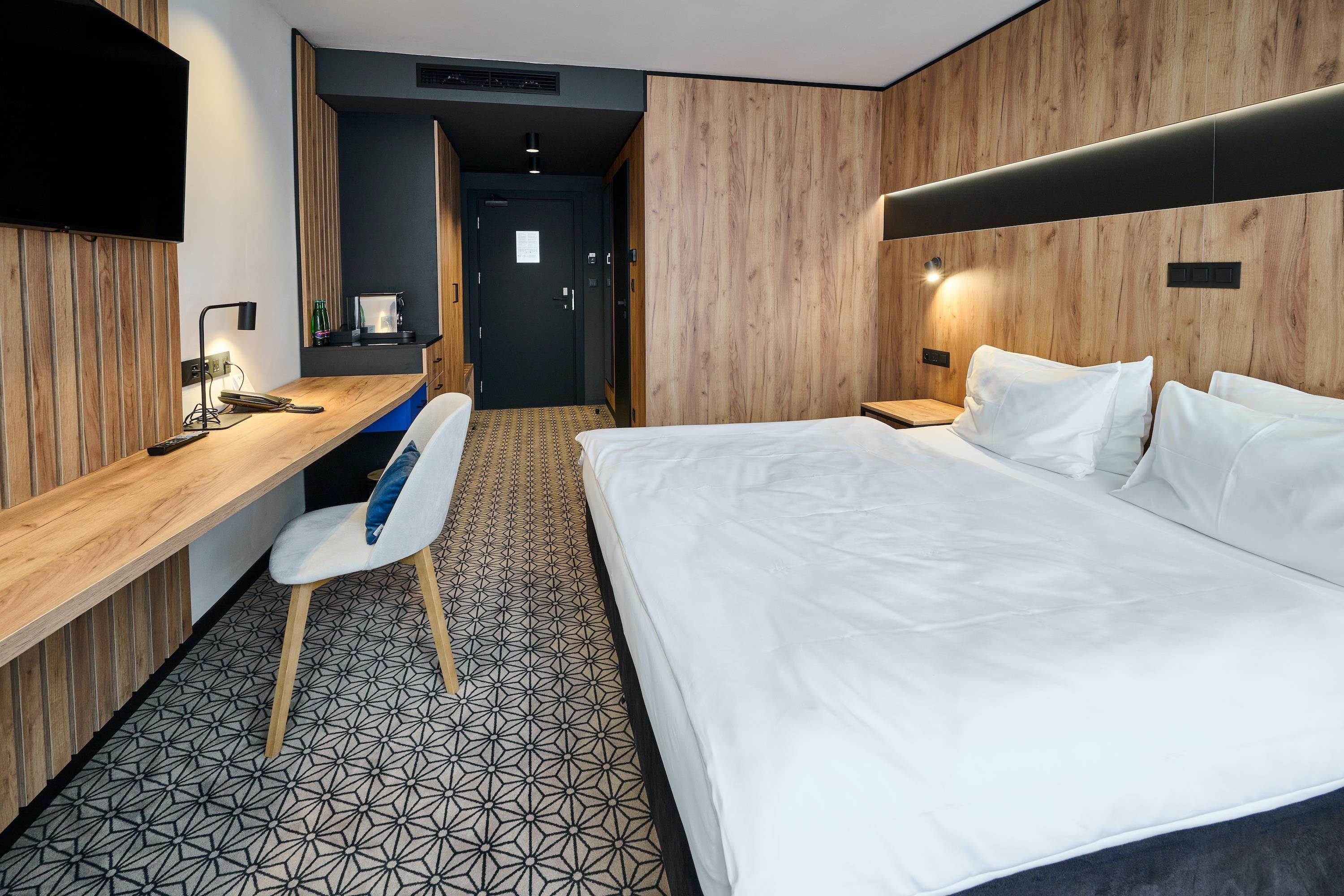 Quarto de hotel com cama, escrivaninha, cadeira e televisão.
