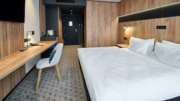 Quarto de hotel com cama, escrivaninha, cadeira e televisão.