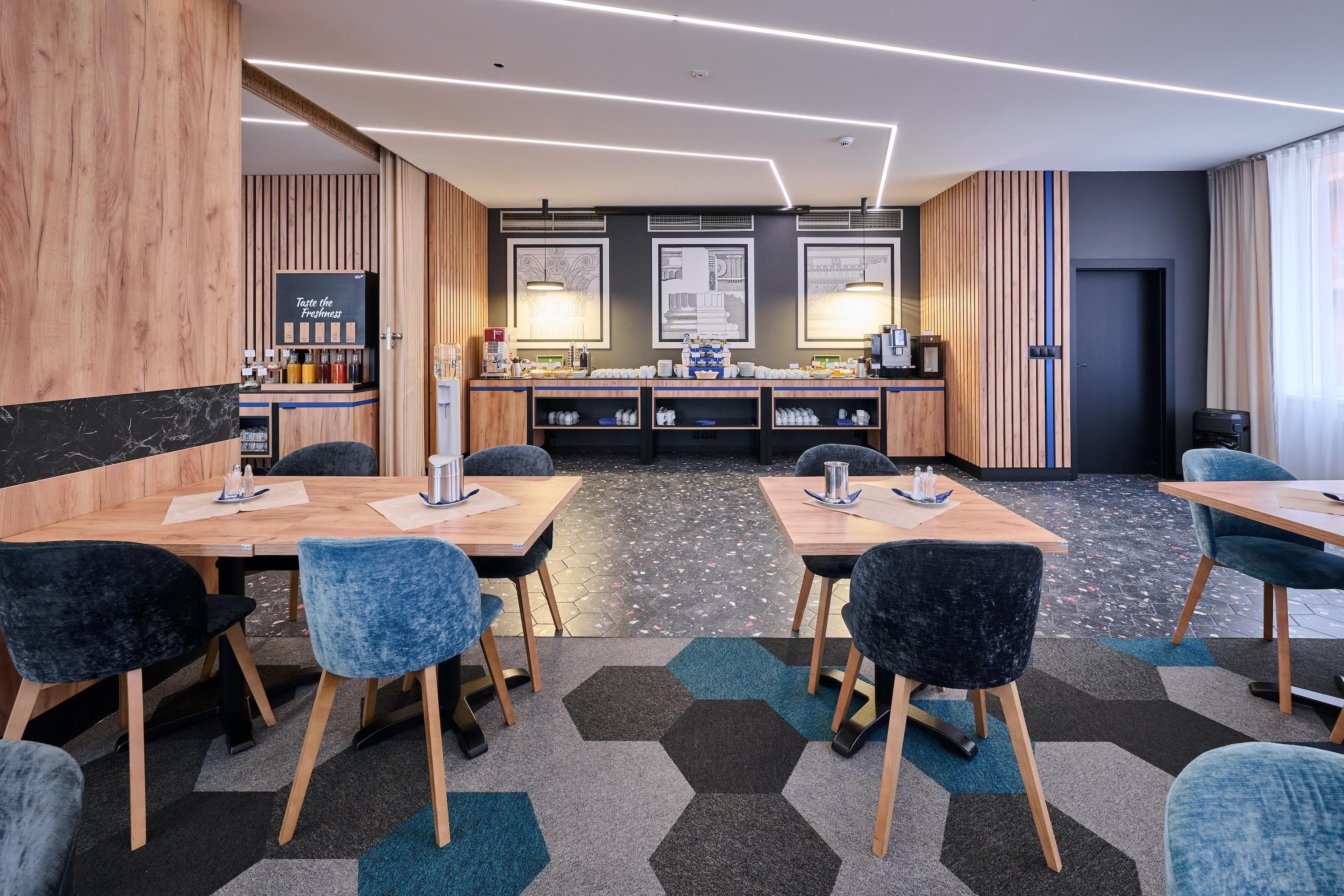 Una habitación de hotel moderna con una pared de acento de madera, una zona de cocina con estación de café y un área de estar con mesas y sillas.