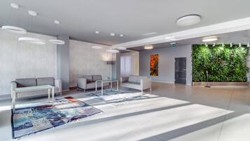 A modern lobby with seating, a patterned rug, and a green wall with plants.