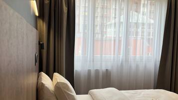 A hotel room with two beds, a window with sheer curtains, and a wall-mounted light.