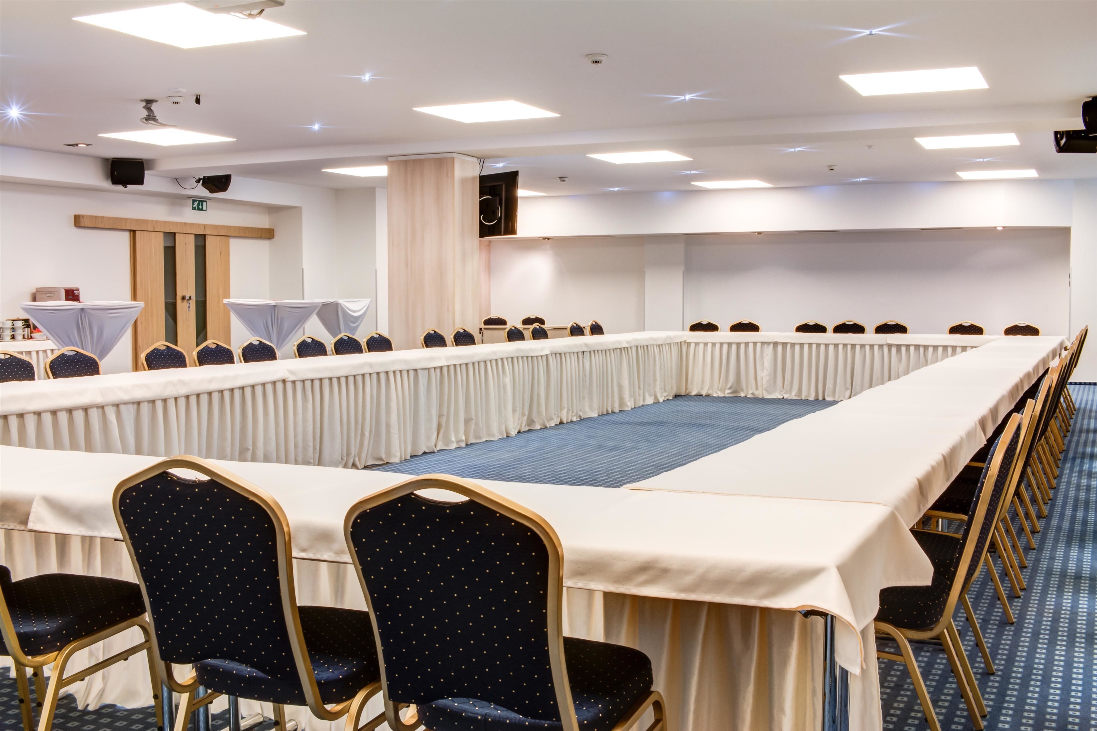 Un salón de conferencias con una larga mesa, filas de sillas, un atril y un orador.