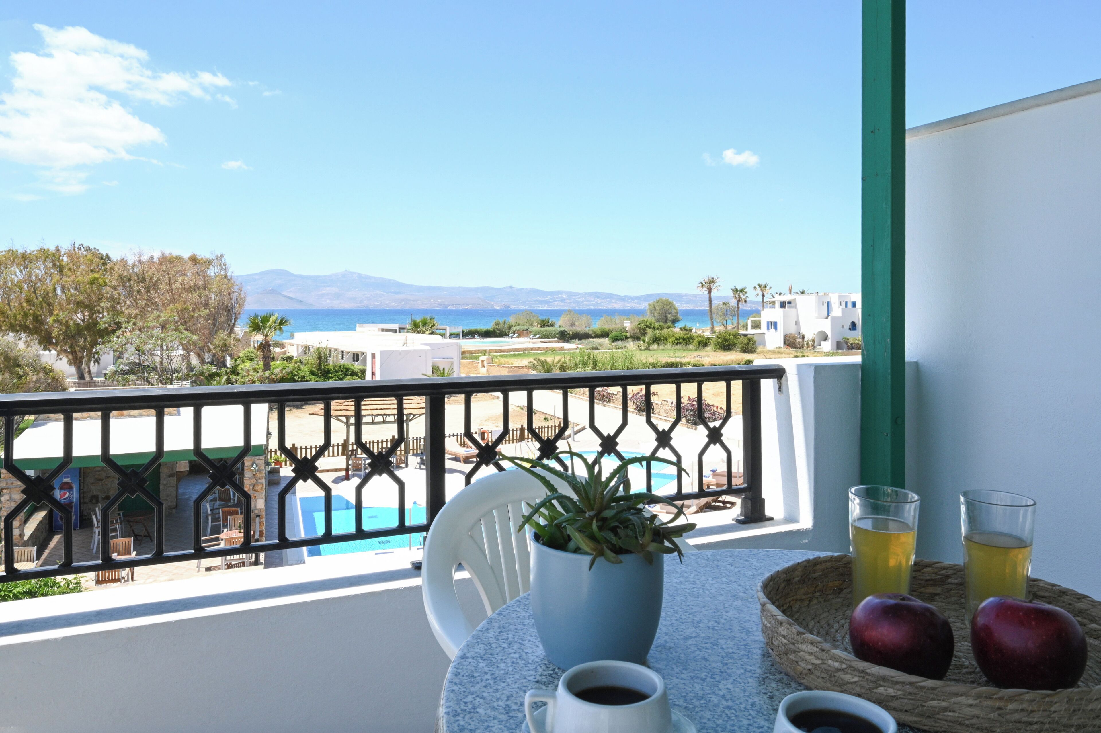 Uma varanda com vista para o mar, uma piscina e um espaço de refeições com mesa, cadeiras e um vaso de planta.