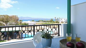 Uma varanda com vista para o mar, uma piscina e um espaço de refeições com mesa, cadeiras e um vaso de planta.