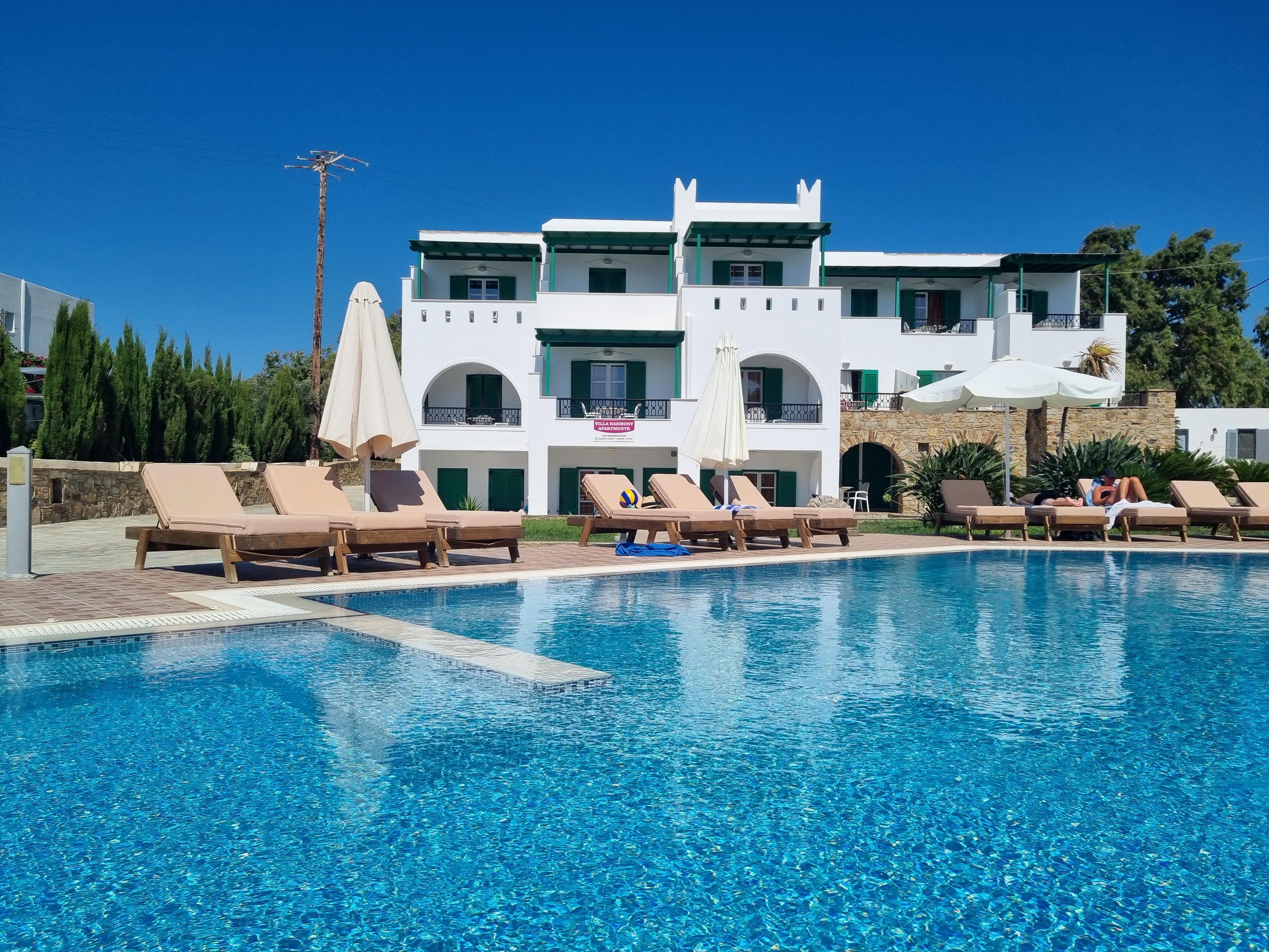 A swimming pool with lounge chairs and umbrellas, surrounded by a building with multiple balconies.