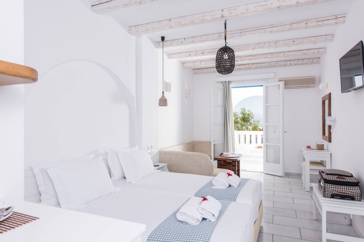 Une chambre d’hôtel avec un grand lit, un petit canapé, un bureau et un balcon avec vue.