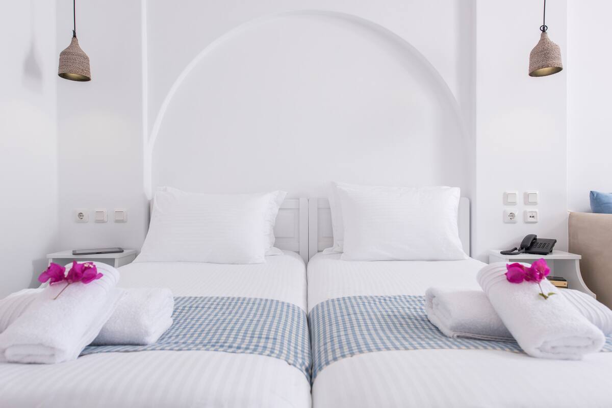 Une chambre d’hôtel avec deux lits, du linge de lit blanc, des couvre-lits à carreaux et une tête de lit blanche en forme d’arc.