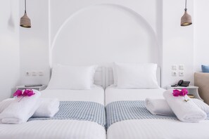 A hotel room with two beds, white linens, checkered bedspreads, and a white arched headboard. - Cycladic Islands Hotel & Spa (Naxos)