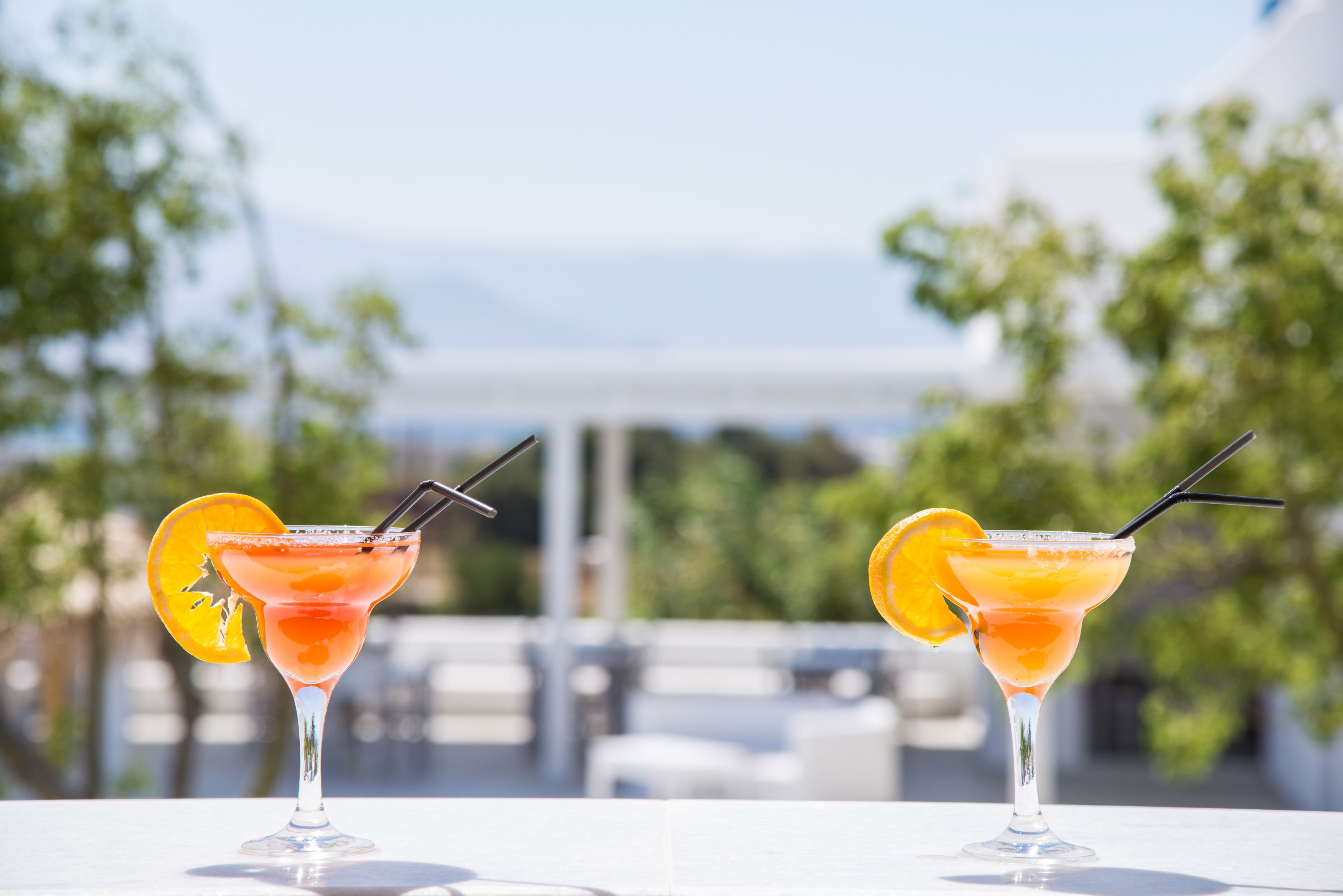 Deux cocktails sur une table blanche, avec un arrière-plan flou représentant un décor extérieur.