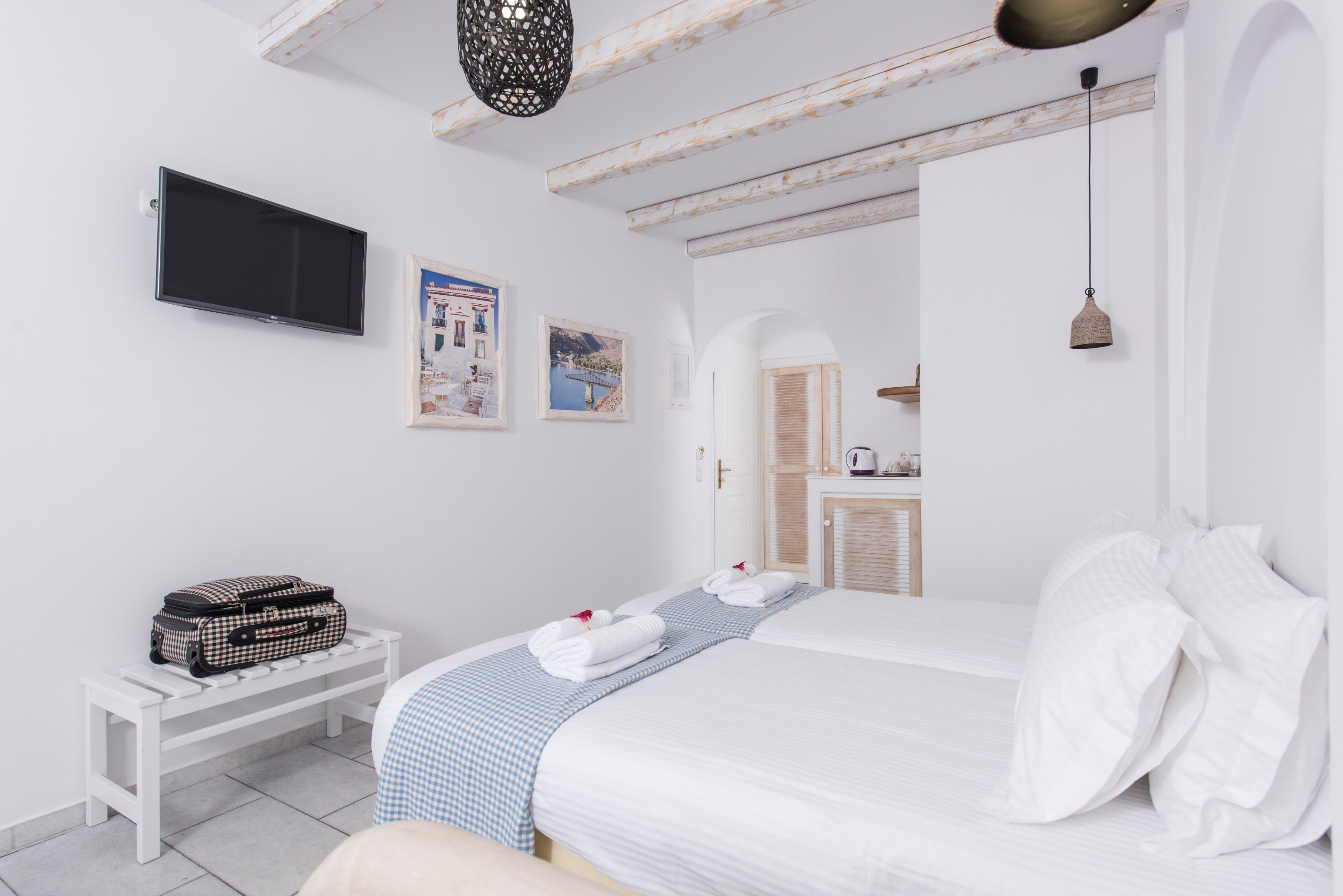 Une chambre à coucher comprenant un lit, un banc, une télévision et une porte donnant sur une autre pièce.