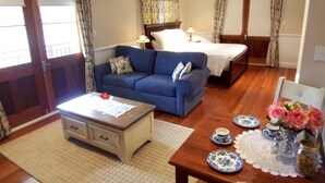 Ein Hotelzimmer mit einem Bett, einem Sofa, einem Esstisch mit Tellern und einer Blumenvase sowie einem Deckenventilator.