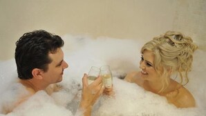 Ein Paar in einer Badewanne voller Schaum, die Gläser halten.