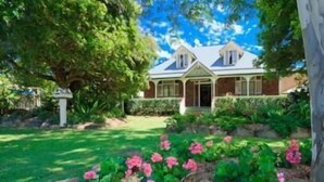 Ein zweistöckiges Haus mit einem gepflegten Garten und einem großen Baum im Vorgarten.