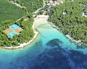 An aerial view of a coastal area with a beach, tennis courts, and a marina.