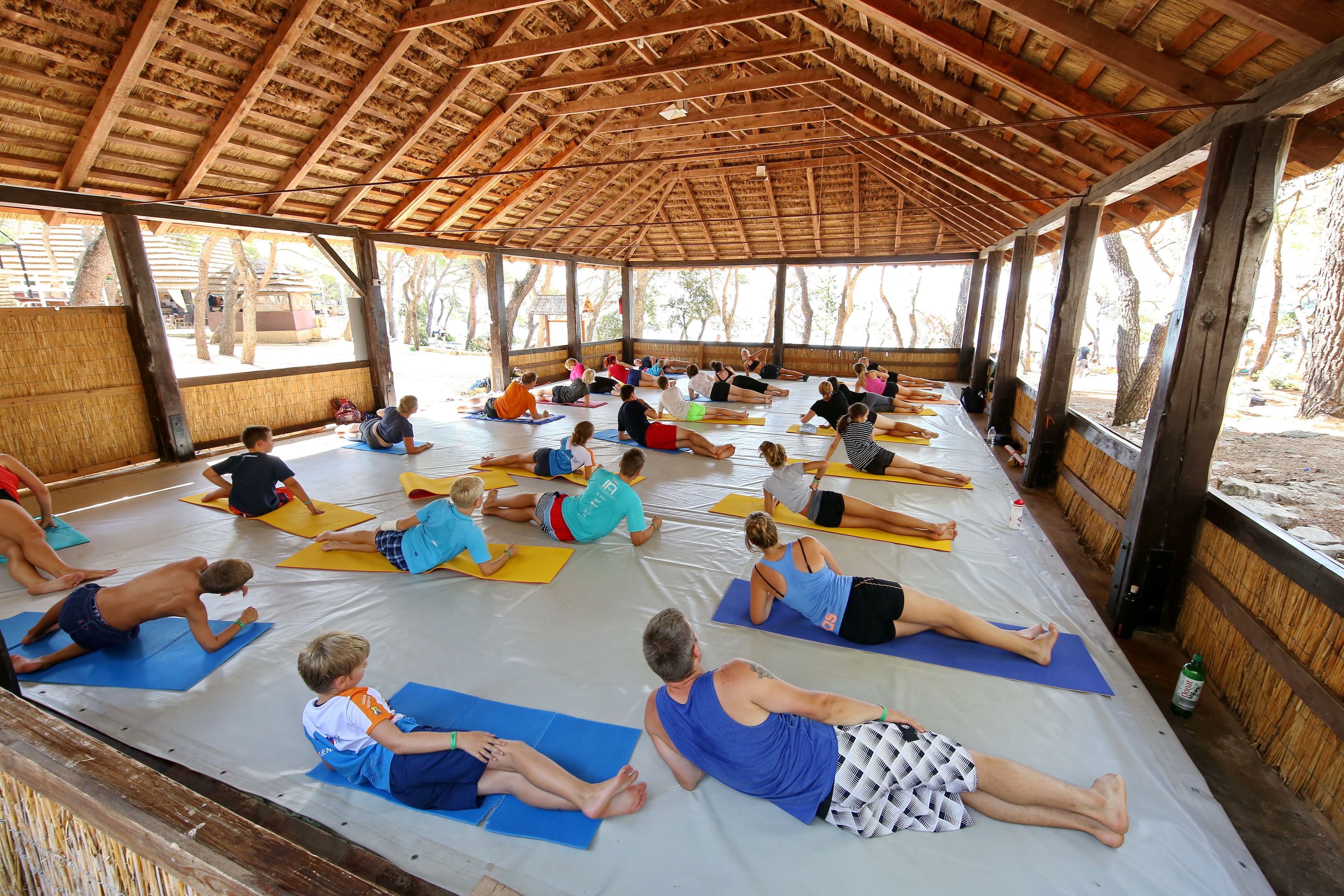 Um grupo de pessoas em tapetes de yoga em área externa coberta com telhado de madeira.