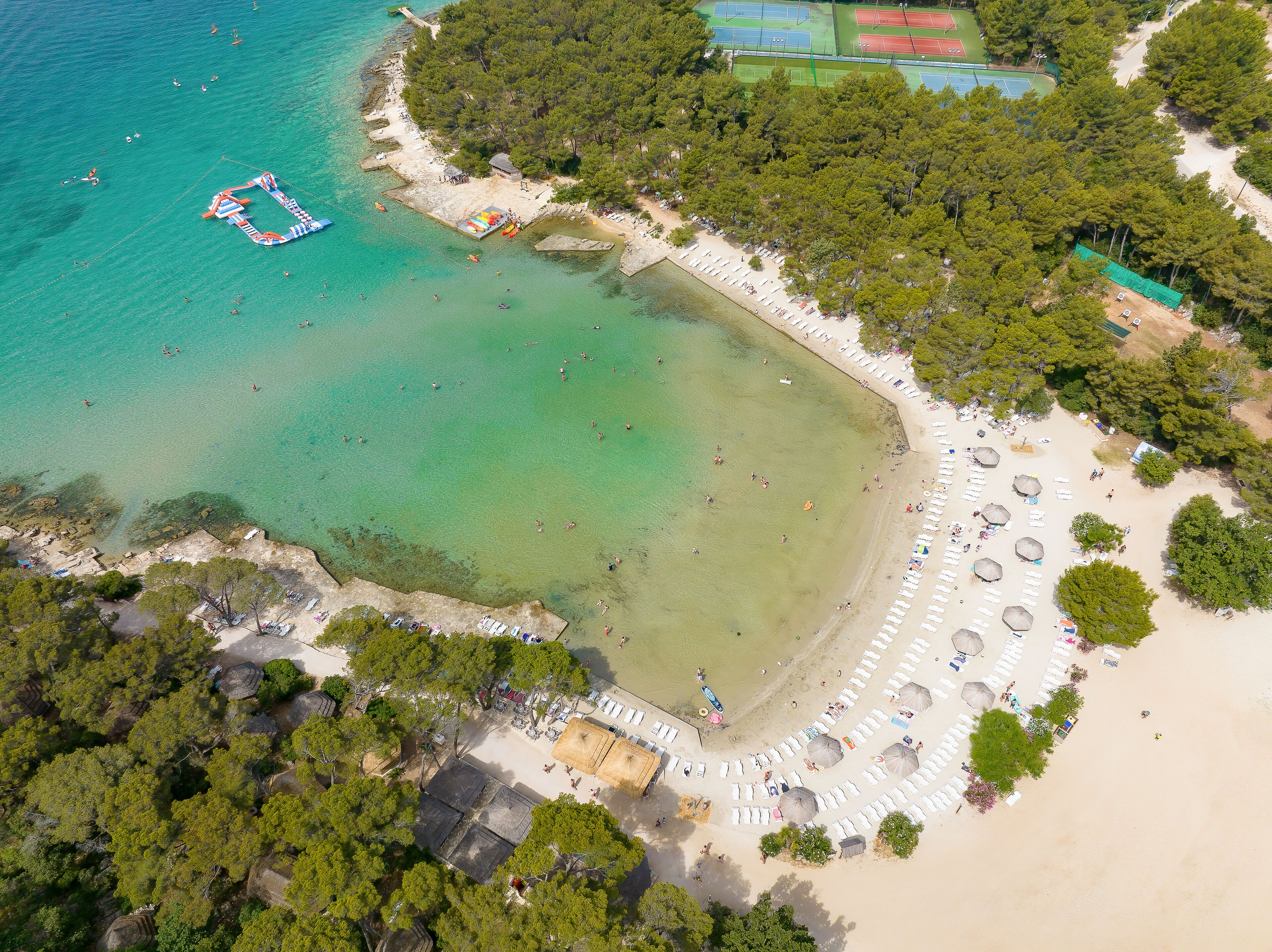 An aerial view of a beach with clear waters, a sandy shoreline, and a row of beach umbrellas.