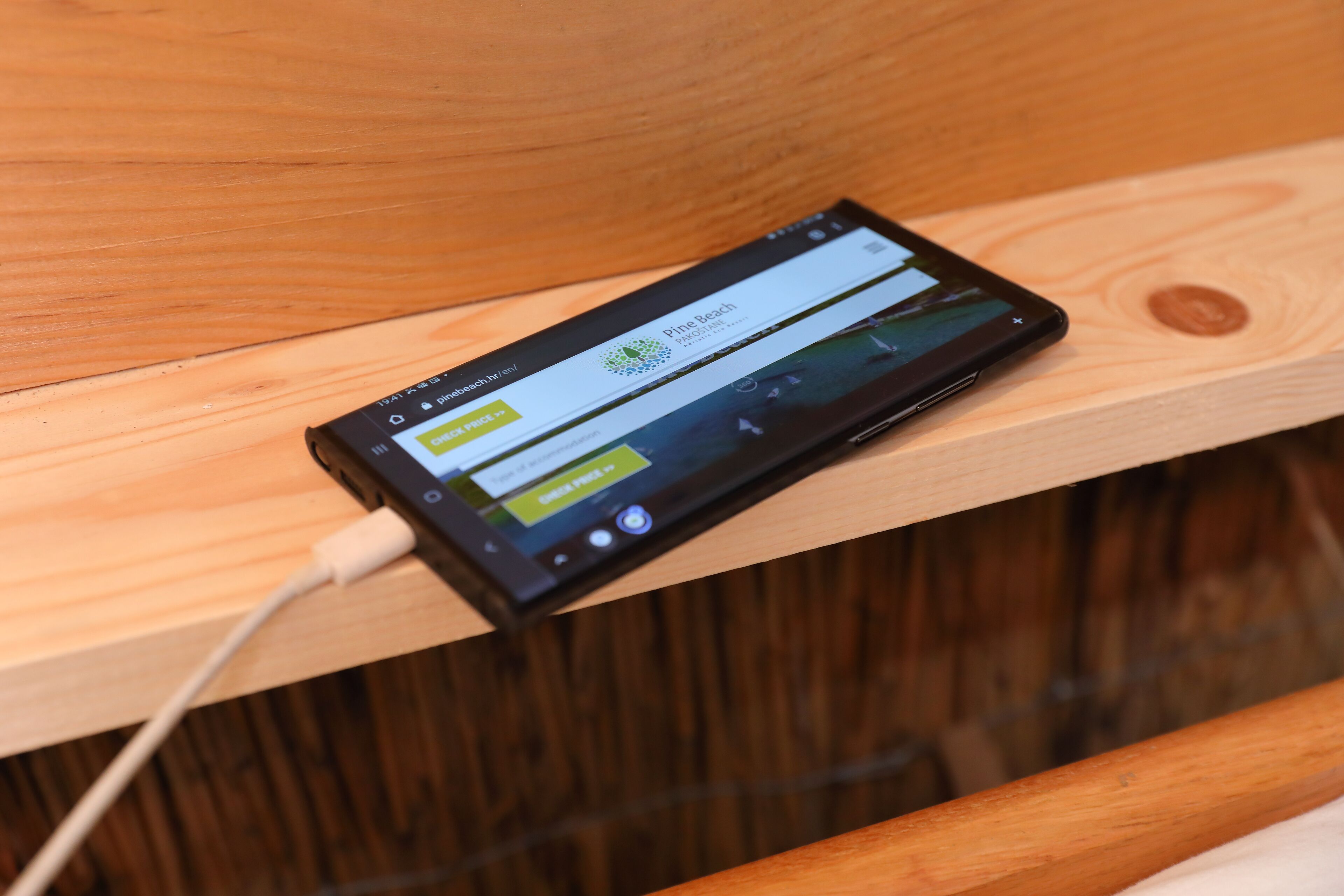 A smartphone on a wooden surface with a charging cable connected.