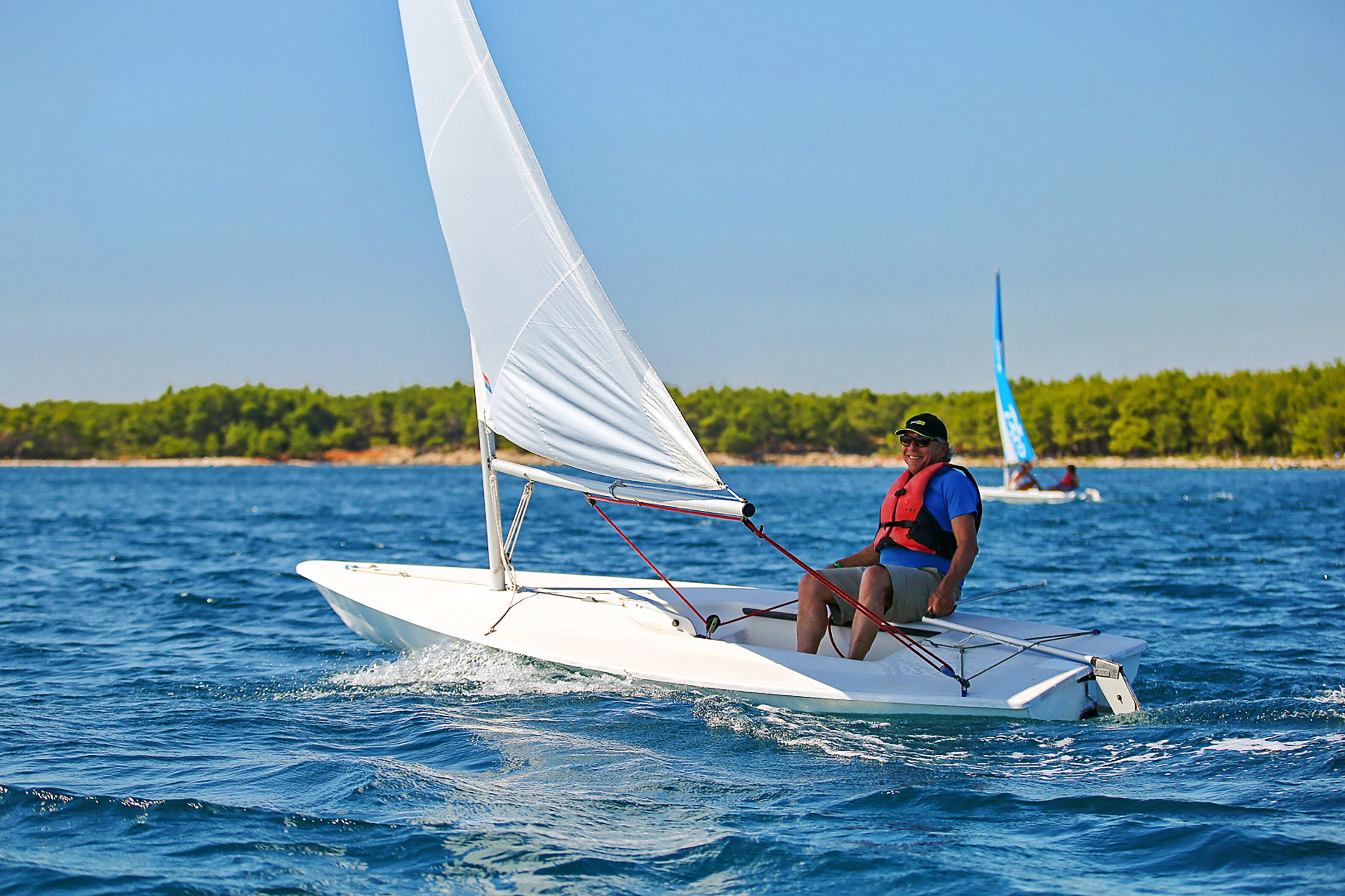 A person sailing a small white sailboat on a calm body of water.