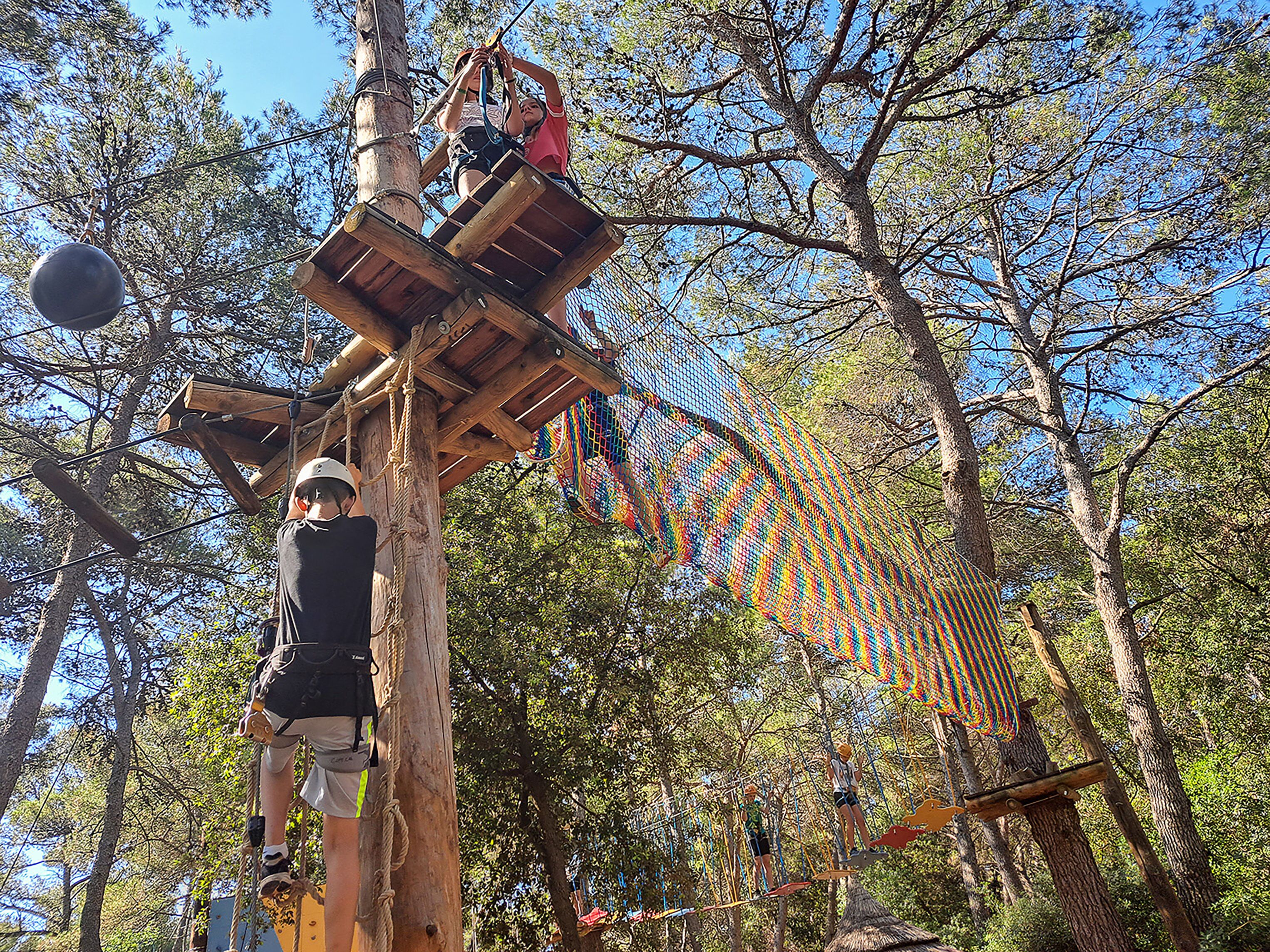 Une structure d’escalade en bois, dotée de cordes et de plateformes, située dans une zone boisée.