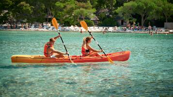 Deux personnes dans un canoë sur une étendue d’eau calme, avec une plage et des parasols en arrière-plan.