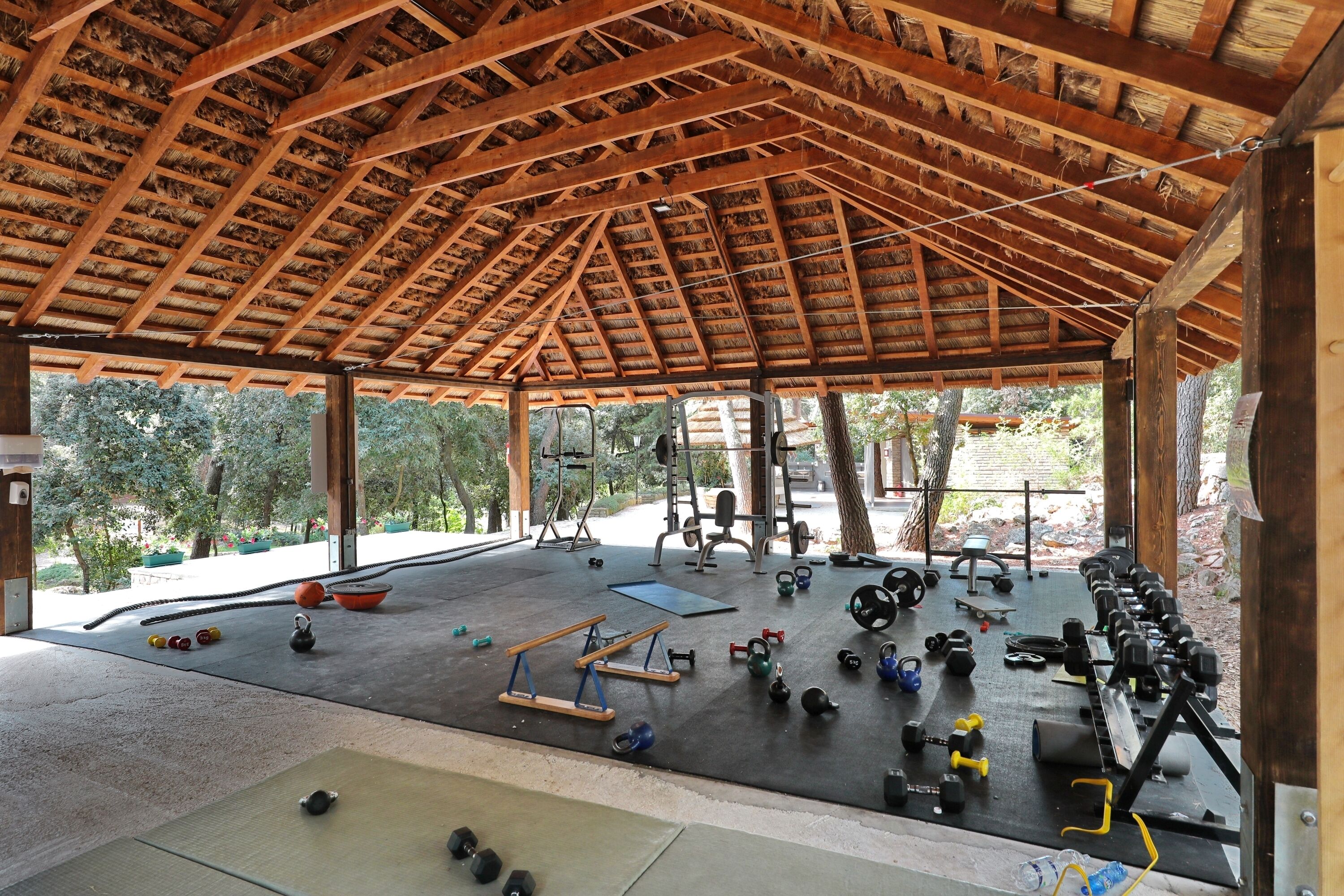 Un gimnasio al aire libre con diversos equipos de ejercicio, incluyendo mancuernas, pesas de contera y una banca.