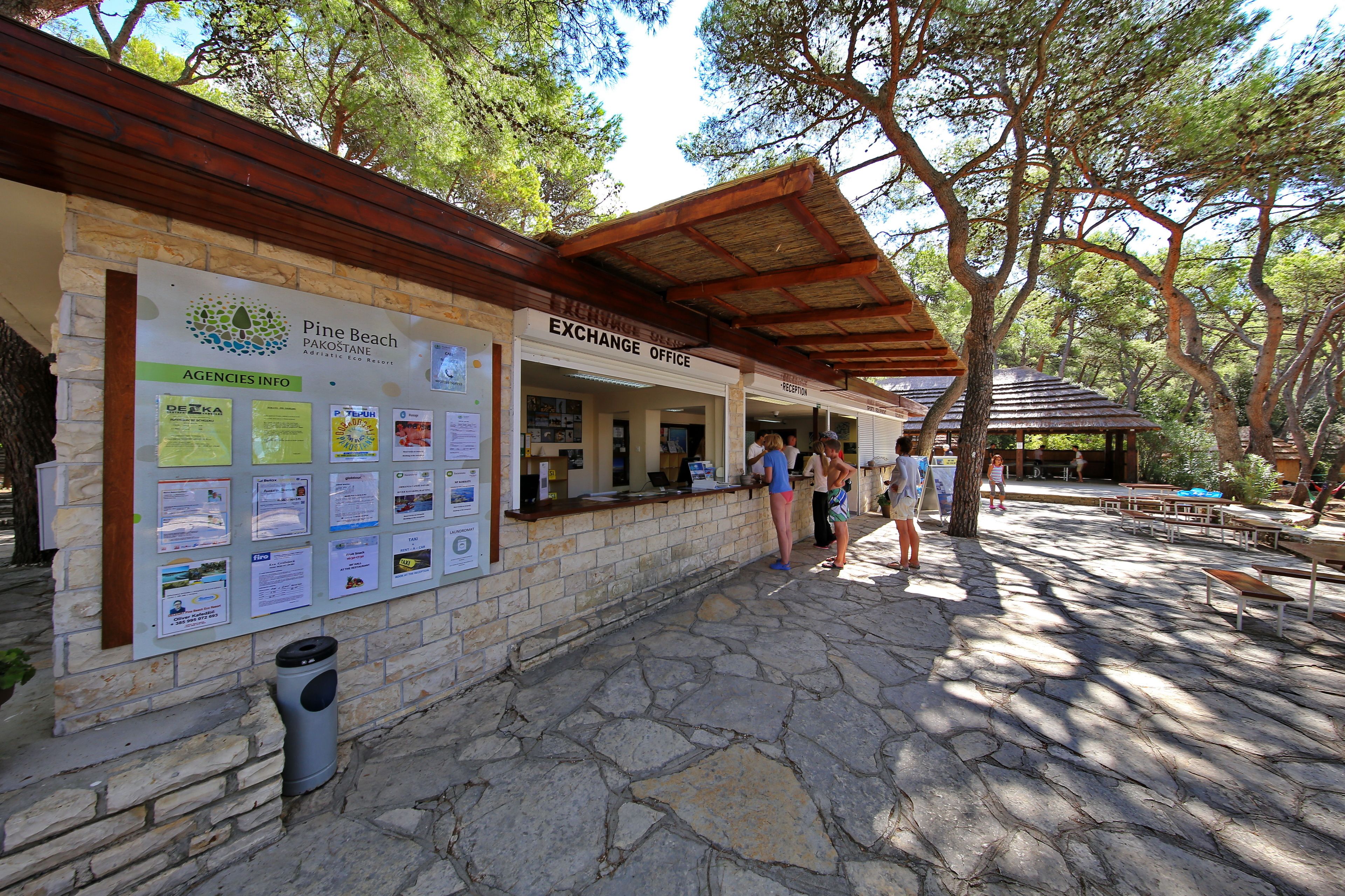 An outdoor exchange office with stone walls and a wooden roof, surrounded by trees.