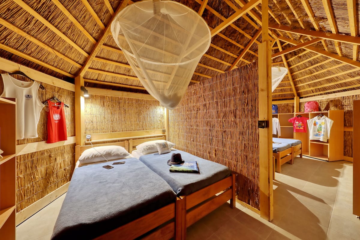 A room with a bed, a hanging mosquito net, and a wardrobe with clothes.