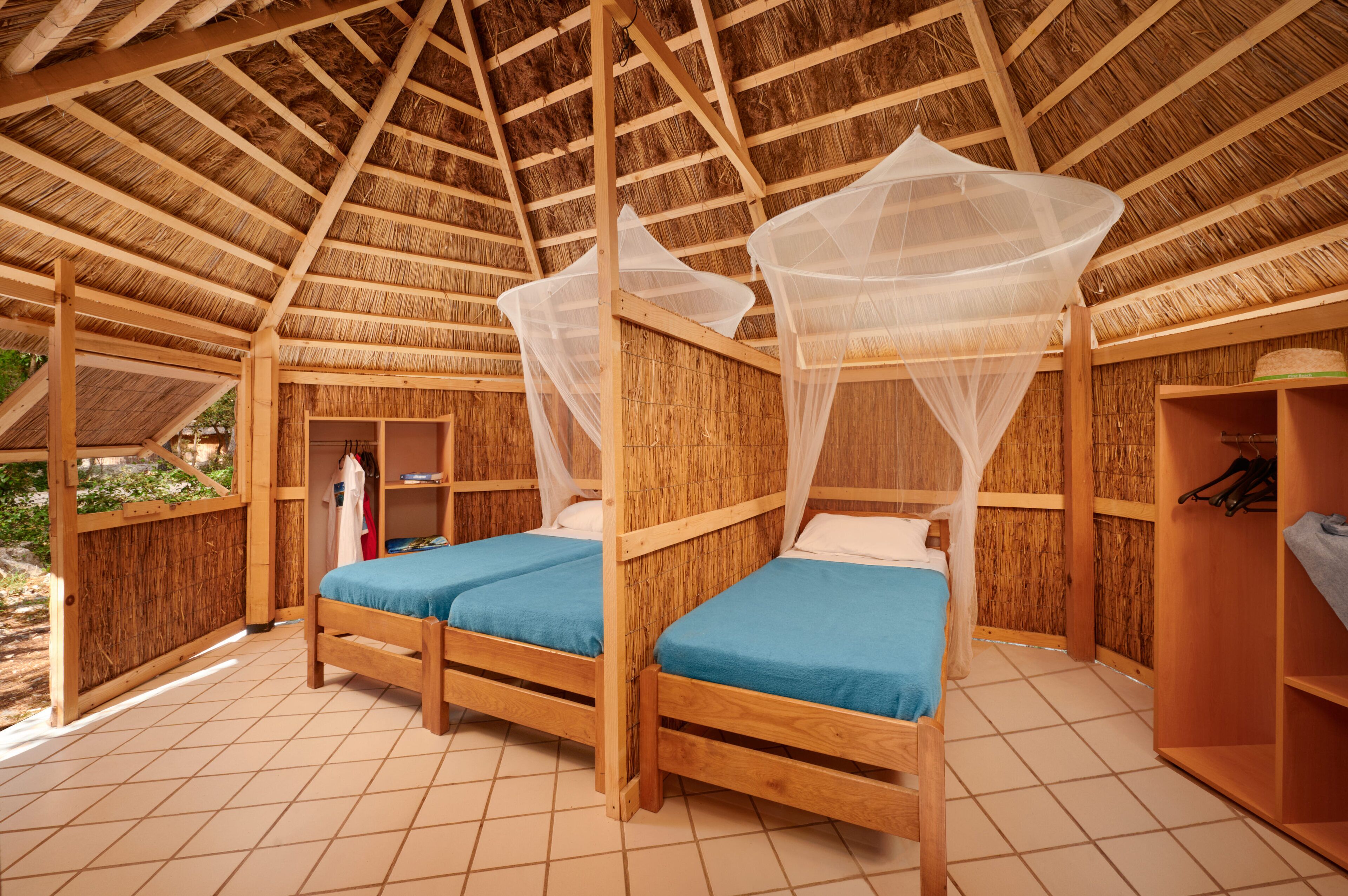 Une chambre avec deux lits en bois, une armoire en bois et une moustiquaire au-dessus des lits.