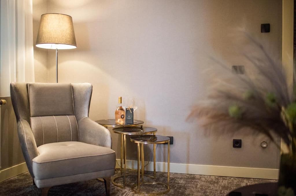 A modern hotel room with a plush armchair, a small round table with a lamp, and a decorative vase.