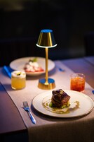 Una mesa de comedor con una lámpara, platos de comida y un vaso de bebida.