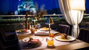 Una mesa de comedor con platos de comida, una lámpara y una vista de un edificio al fondo.
