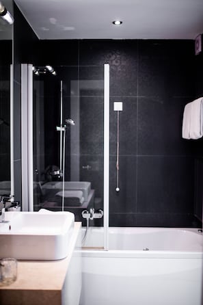 A modern bathroom with a glass shower enclosure, a white bathtub, and a vanity with a sink. - Crystal Hotel Belgrade (Belgrade)
