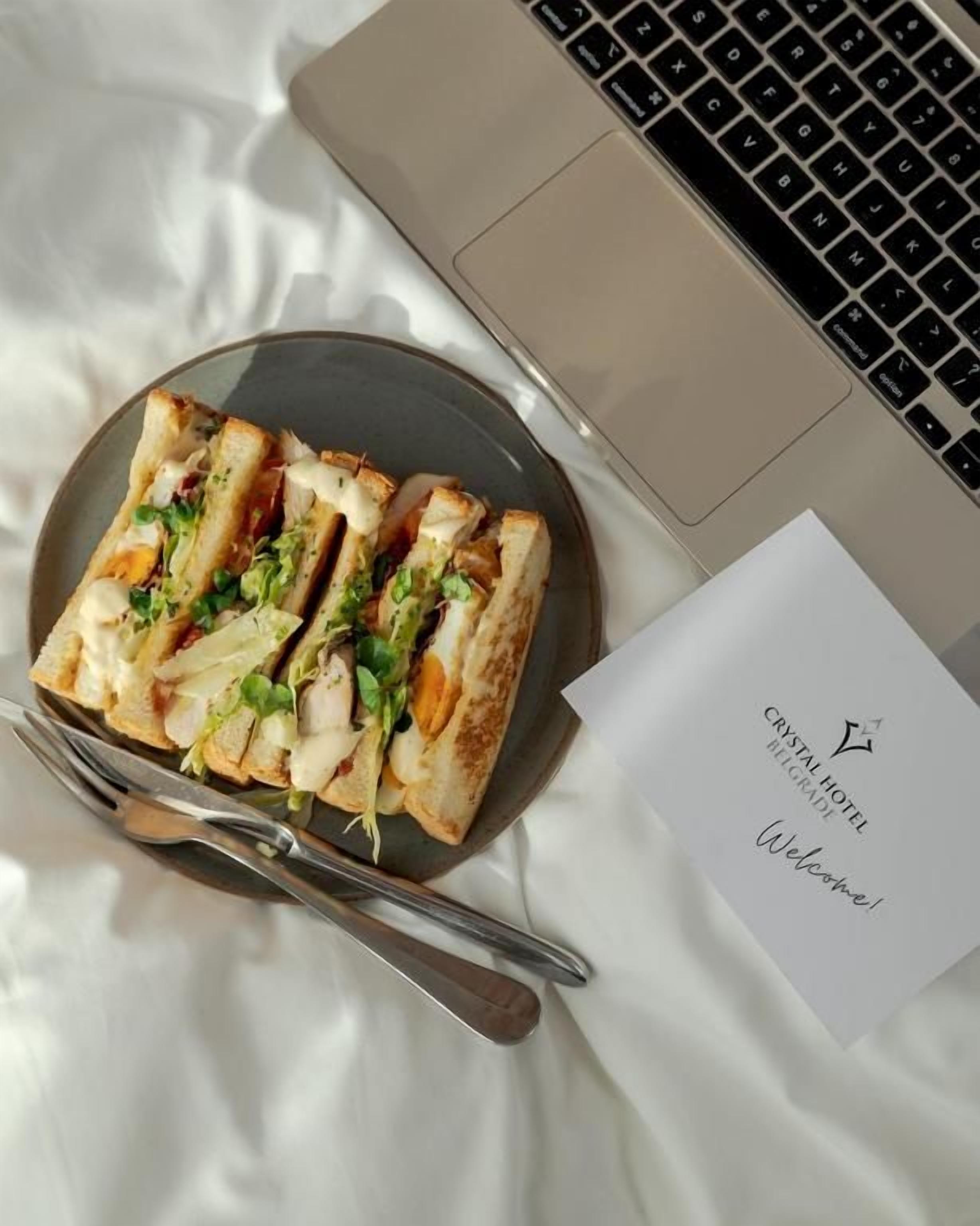 Un plato de comida, una computadora portátil y una tarjeta de bienvenida sobre una cama.