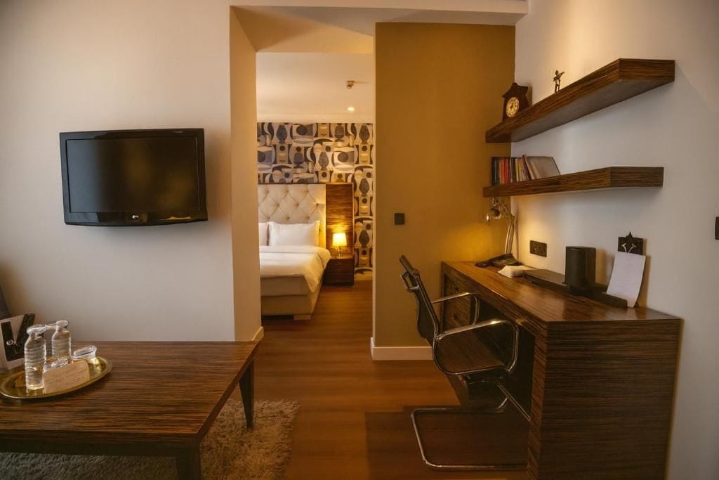Une chambre d’hôtel comprenant un lit, un bureau avec une chaise, une télévision et des étagères avec des livres et une horloge.