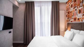 Habitación de hotel moderna con una cama grande, un televisor de pantalla plana y un ventanal con cortinas.