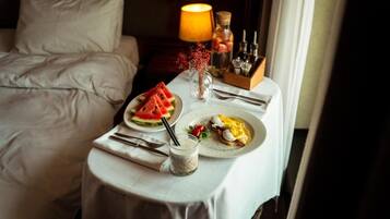 Una mesa de desayuno ordenada con platos de comida, un jarrón con flores secas y una lámpara en una mesita de noche de un cuarto de hotel.