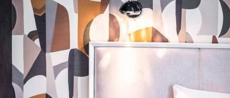A modern hotel room with a bed, bedside table, and a wall with abstract patterns.