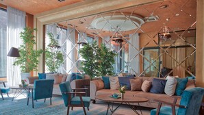 Una sala de estar moderna con un sofá modular, sillones y una mesa de centro. Hay plantas en macetas y un ventanal que proporciona luz natural.