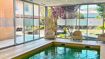 An indoor swimming pool with clear glass walls, a ceiling with a geometric pattern, and a view of the outside.