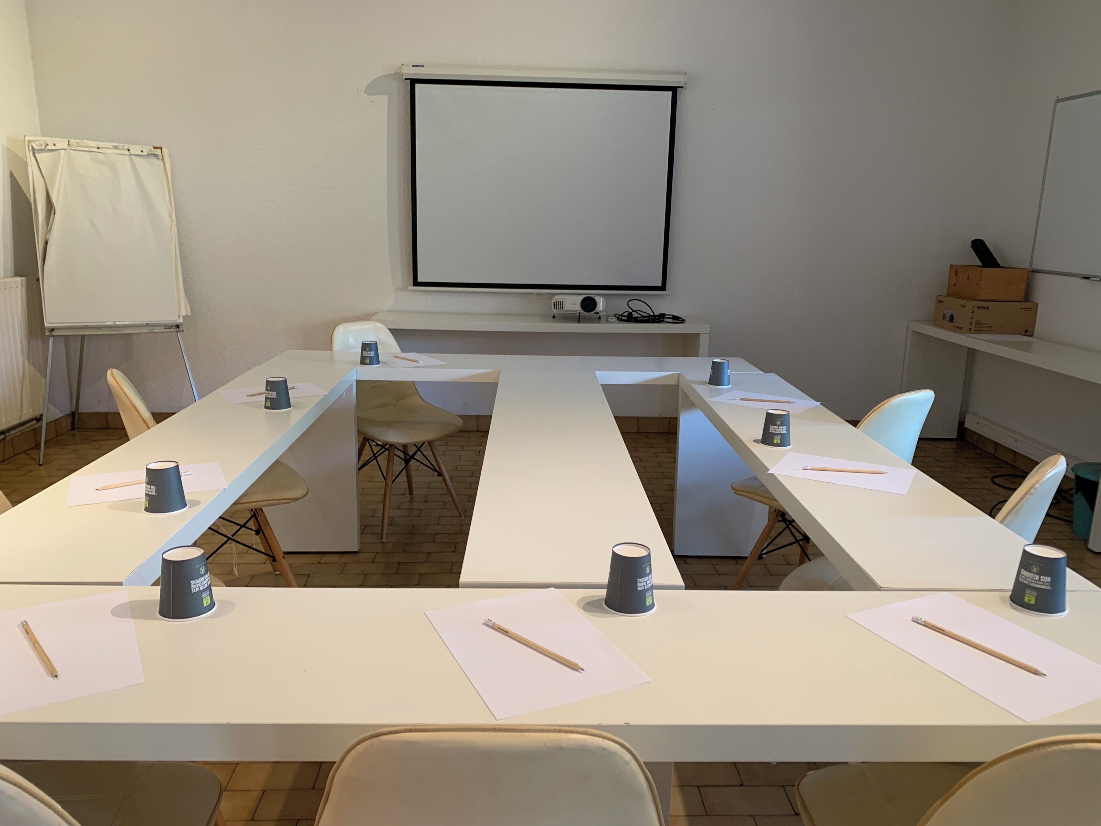 Een vergaderruimte met een lange tafel, stoelen, een projectiescherm en een whiteboard.