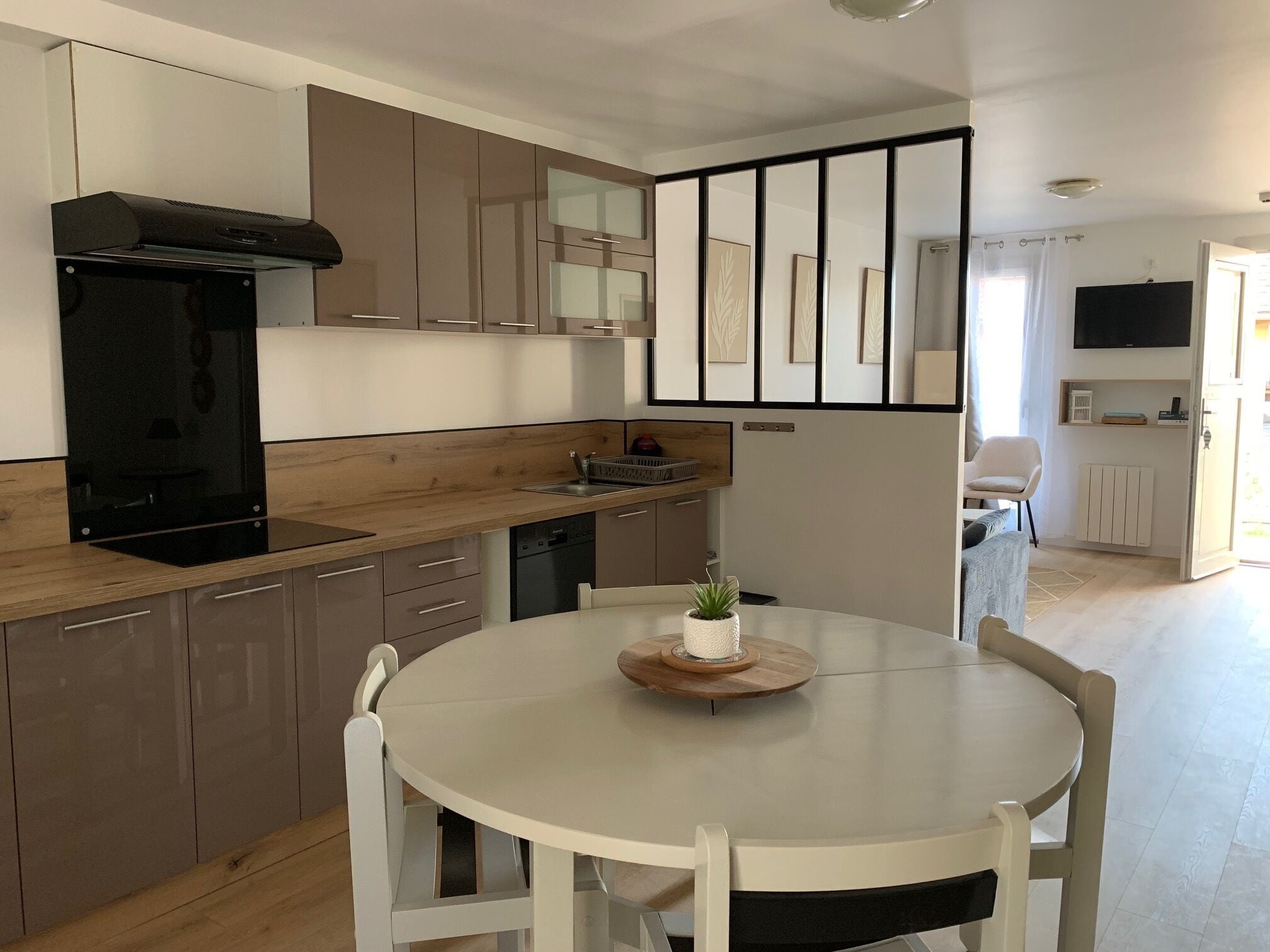 A modern kitchen with a round dining table, white chairs, and a small potted plant.