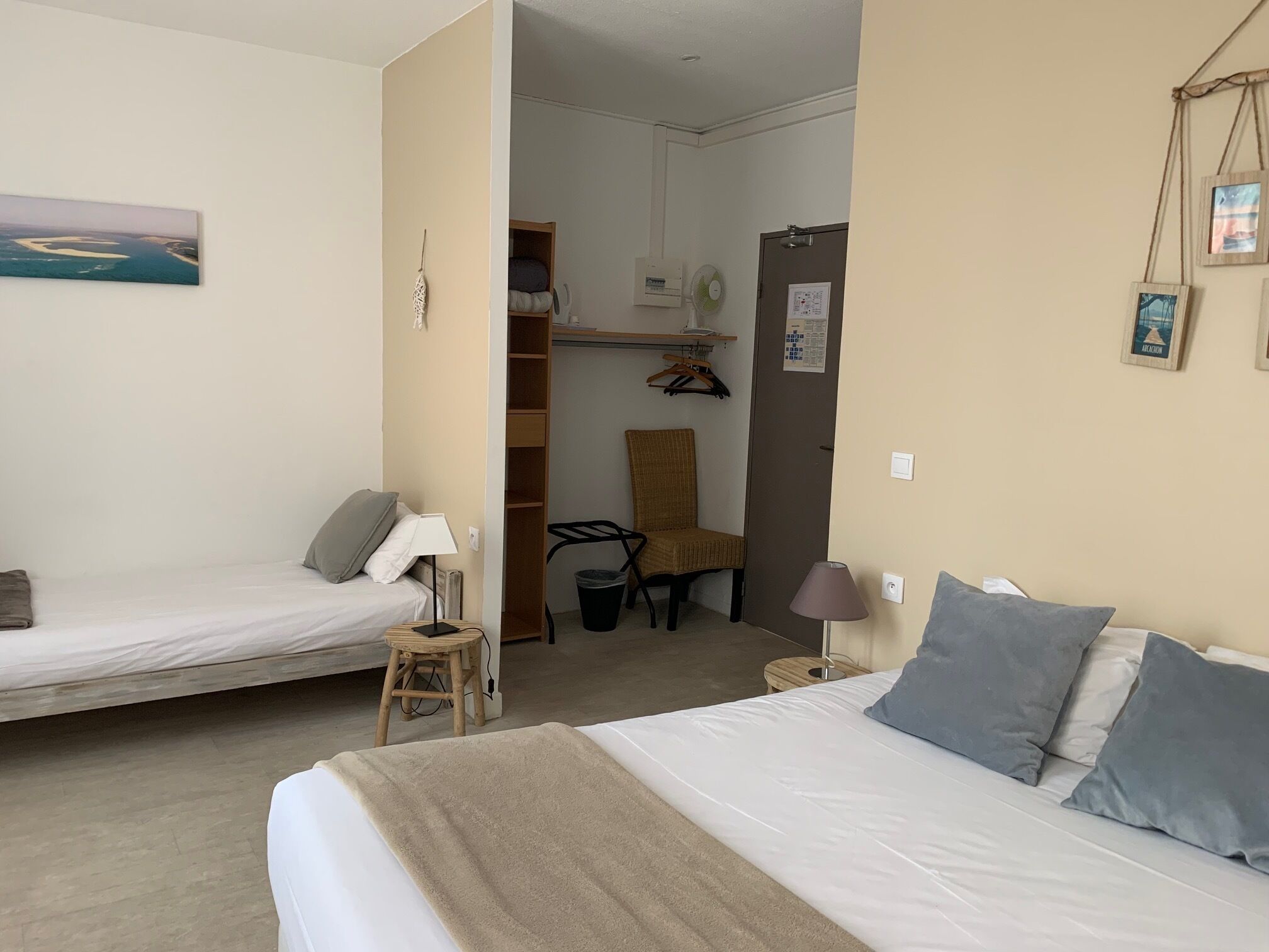 A room with two beds, a chair, a small stool, a lamp, and a wall-mounted fan.