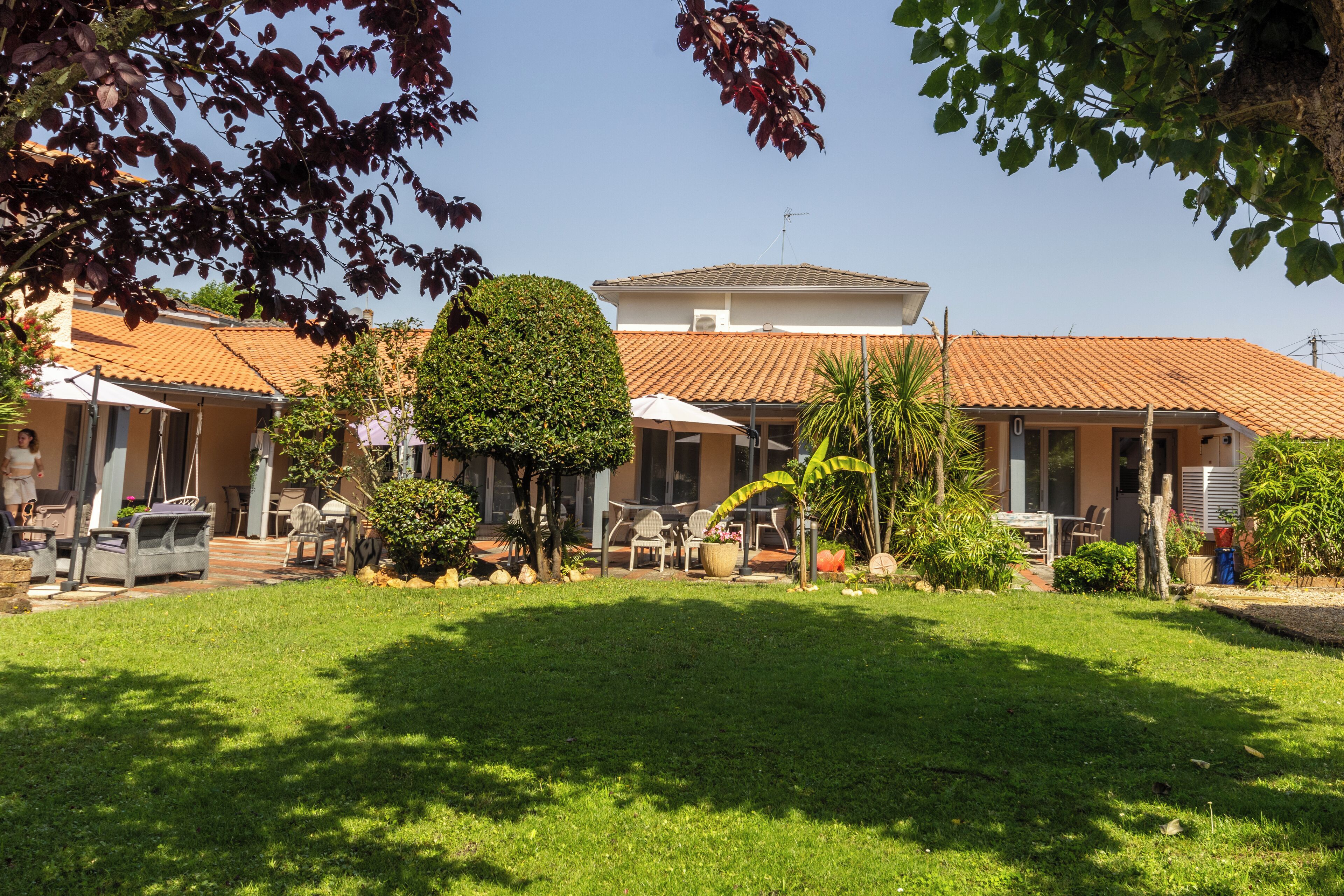 Una propiedad residencial con un césped bien cuidado, un patio con mobiliario exterior y un tejado de tejas.