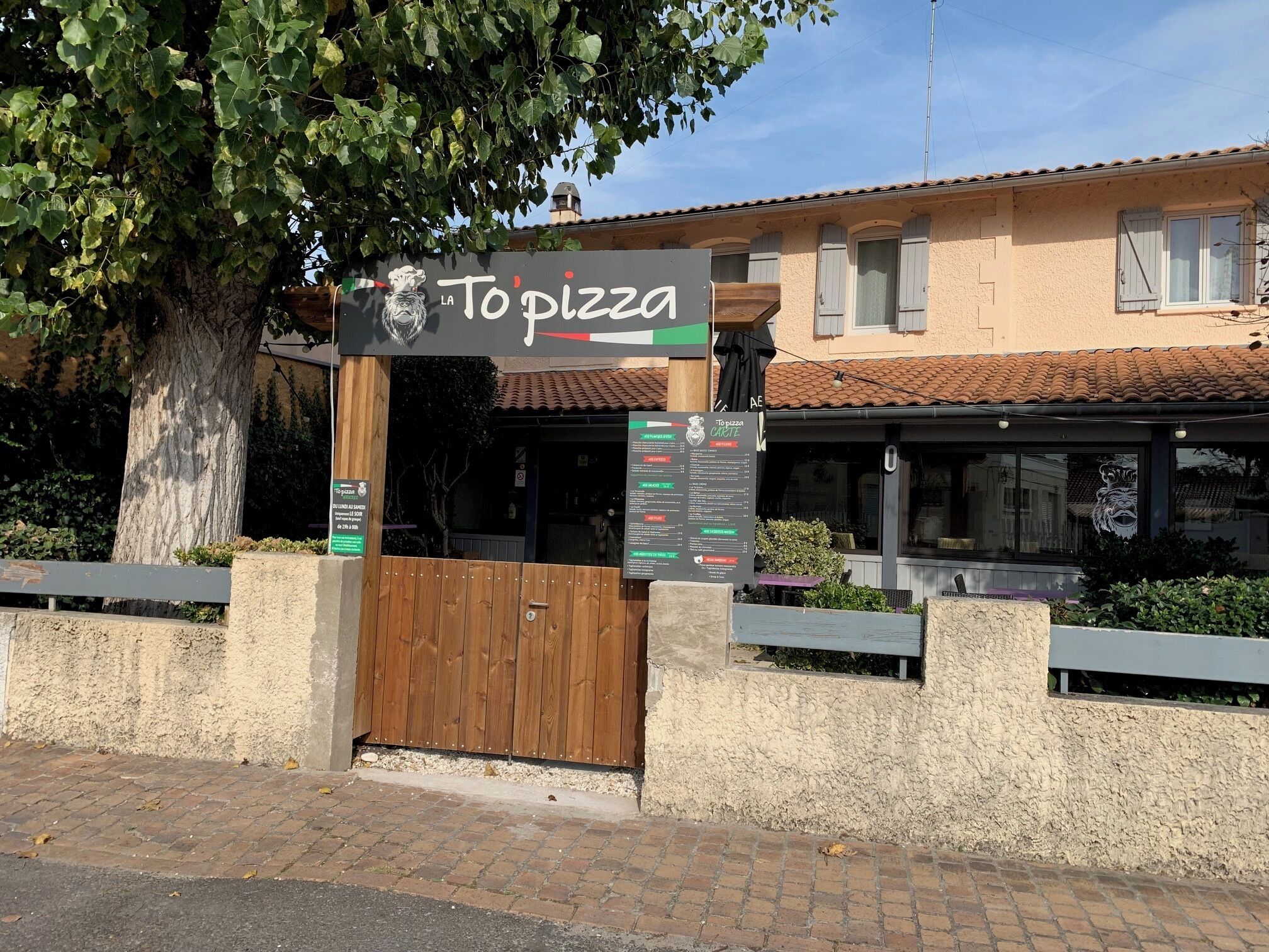 A restaurant named 'To pizza' with a wooden gate and a menu board.
