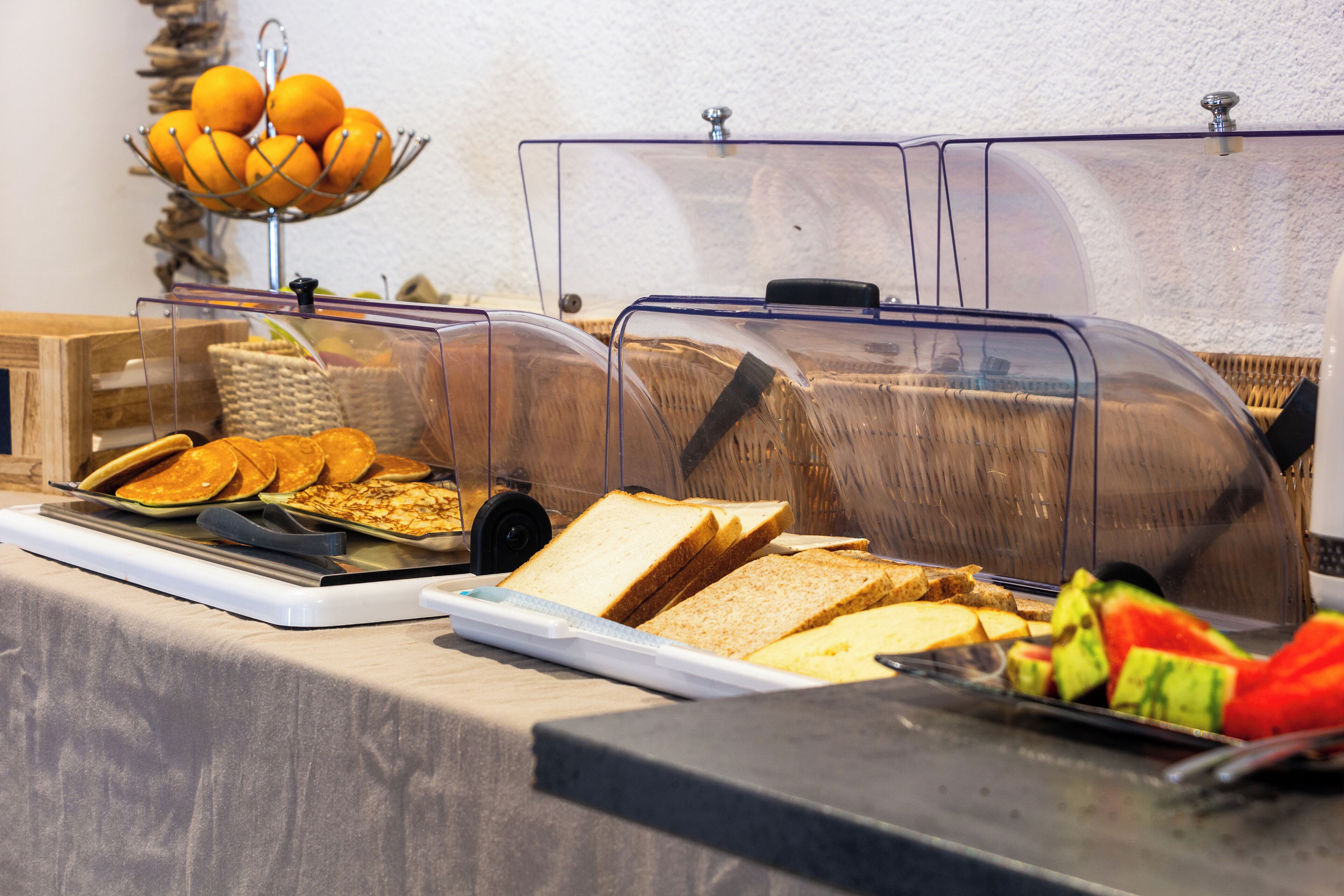 A buffet with various food items including bread, pancakes, and fruits.