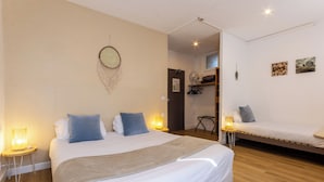 Un dormitorio con una cama grande, una cama más pequeña, una mesita de noche con lámpara, un adorno en la pared y una puerta que da a otra habitación.