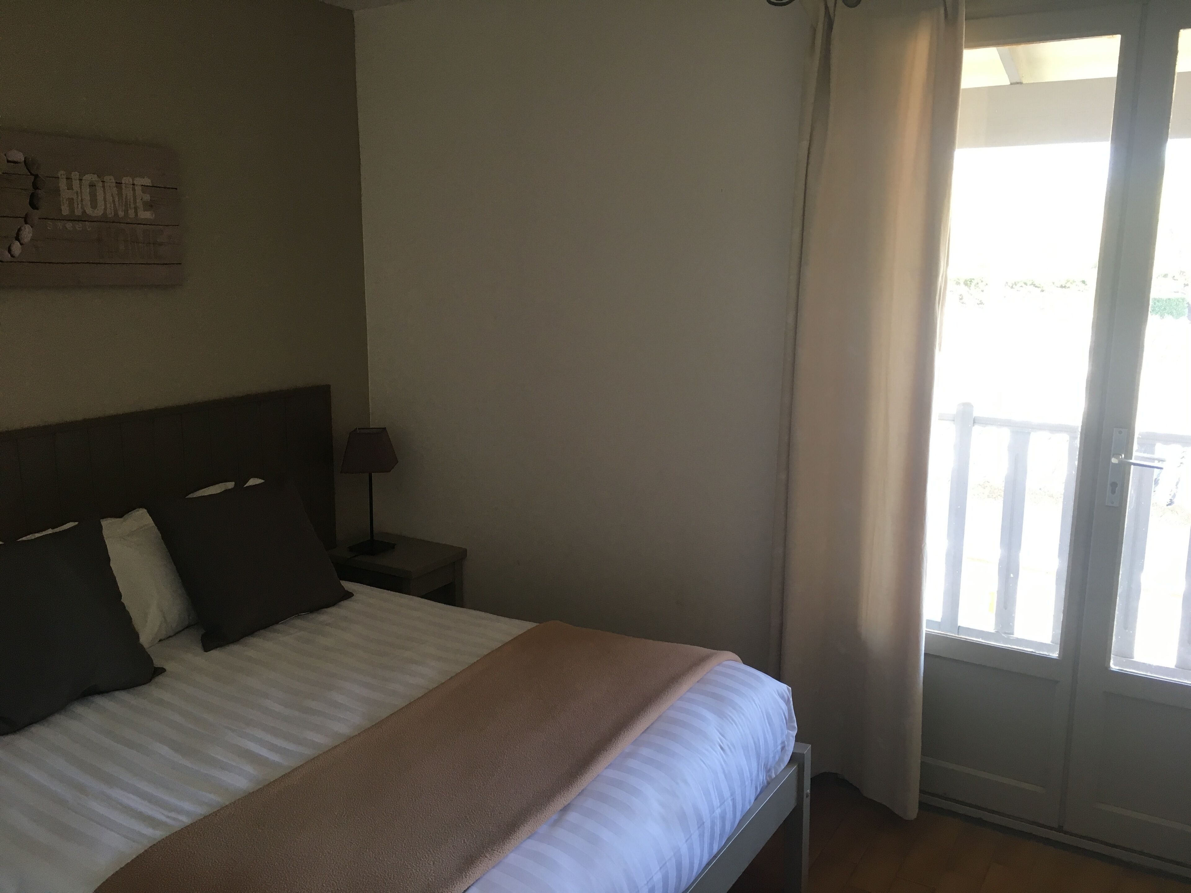 A bedroom with a bed, a nightstand, a lamp, a window with curtains, and a 'HOME' sign on the wall.