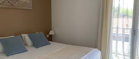 A bedroom with a large bed, a wall-mounted map, a window with sheer curtains, and a view of the outside.