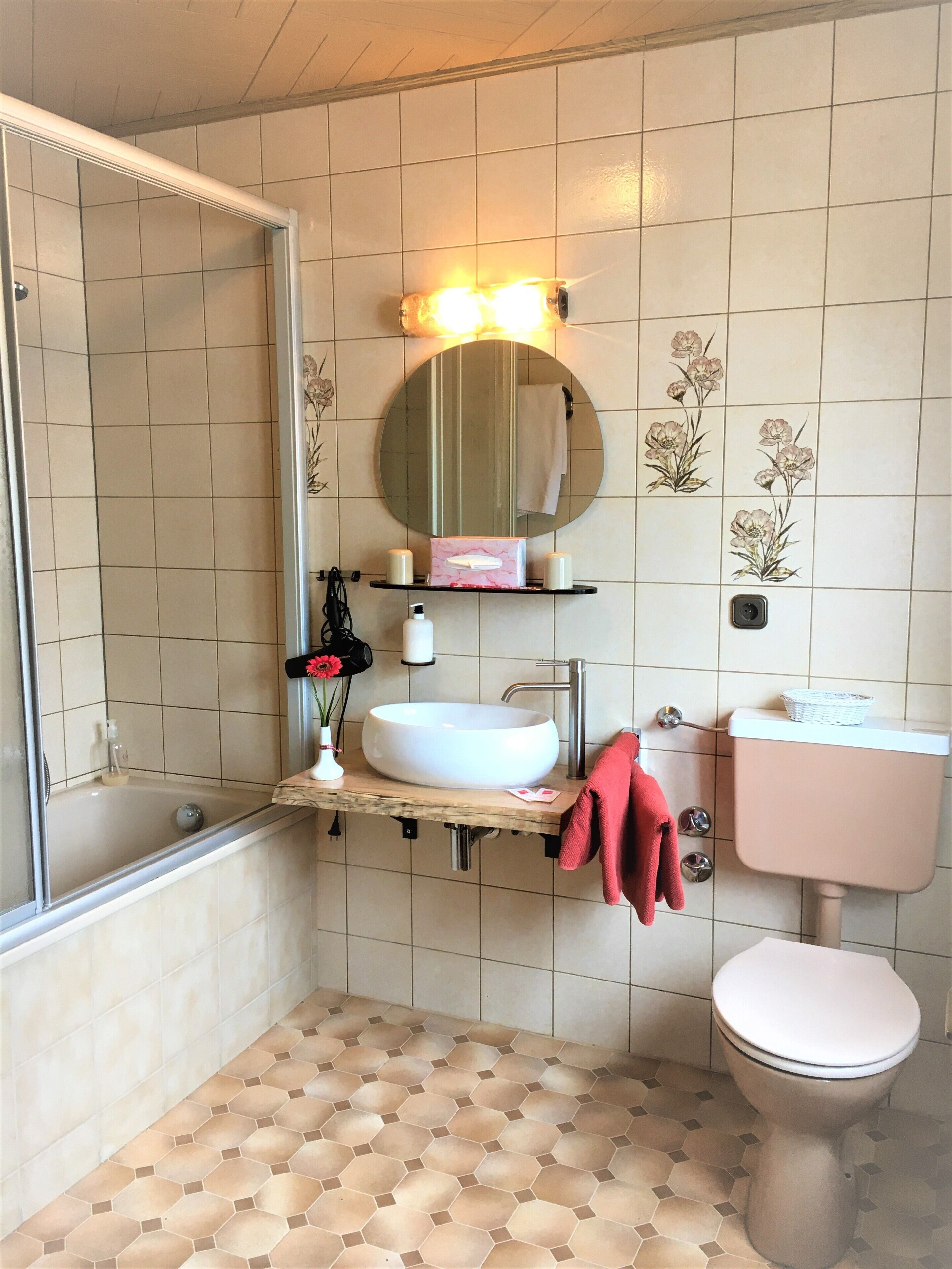 Un baño con lavamanos blanco, espejo redondo y retrete.