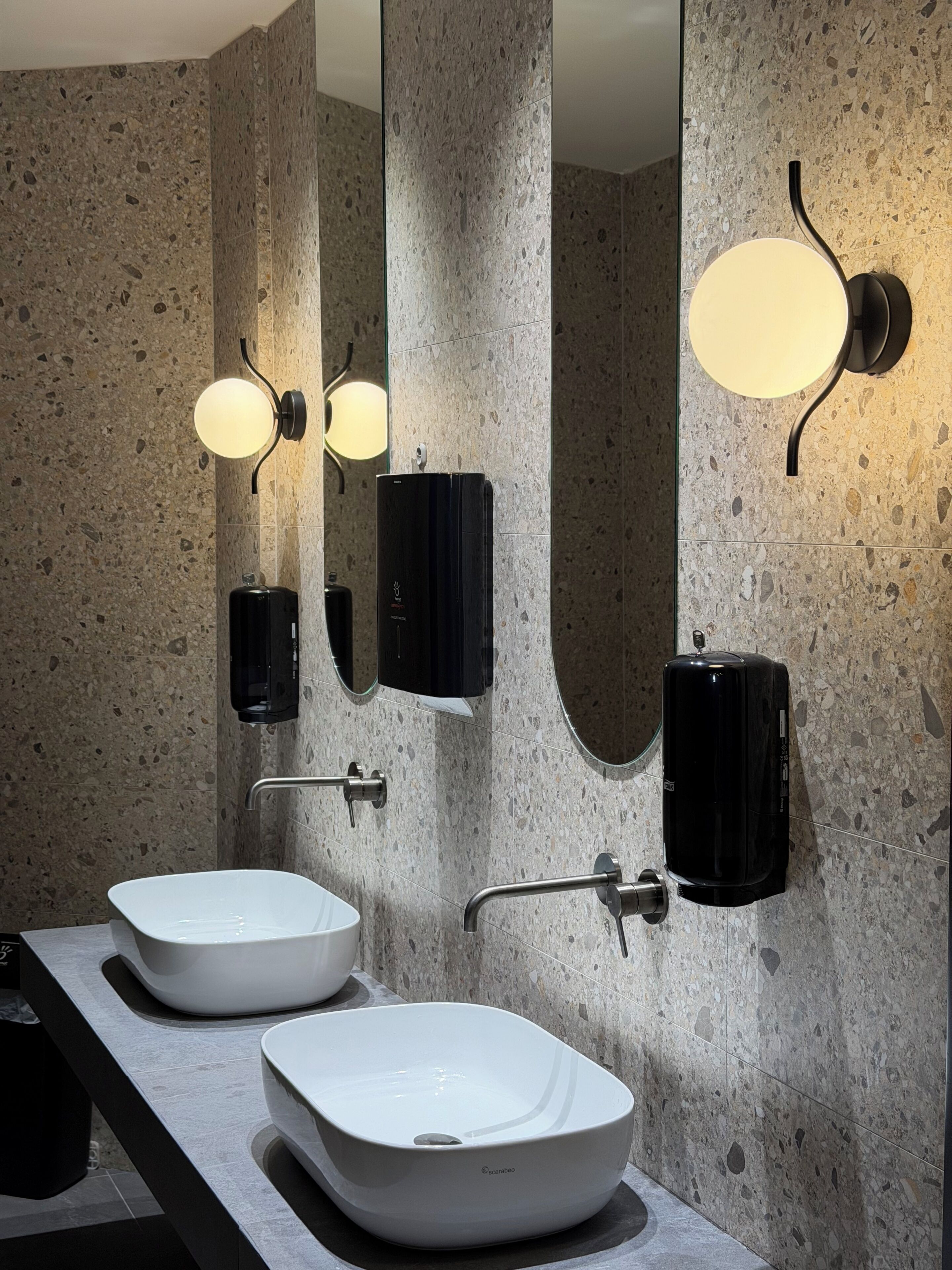 Un baño moderno con dos lavamanos blancos, un espejo grande e iluminación empotrada.